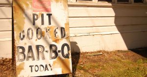white sign with peeling paint that reads, "Pit Cooked Bar-B-Q today"