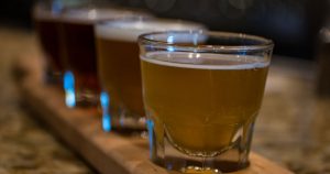 close up shot of 4 glasses of various beers on a wooden serving tray.