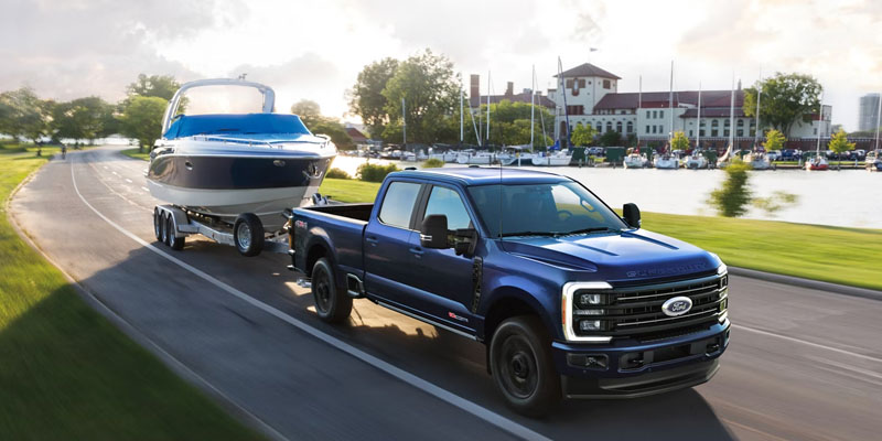 A blue Ford Super Duty truck towing a boat near a marina.